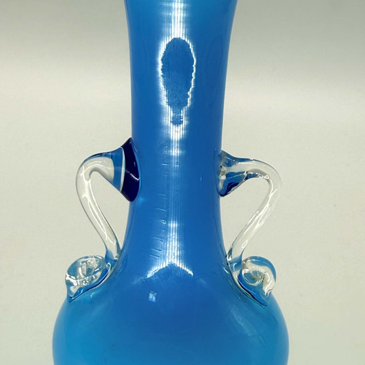 A blue glass vase with a flared round base, a narrow neck, and two clear glass handles, shown against a light neutral background.