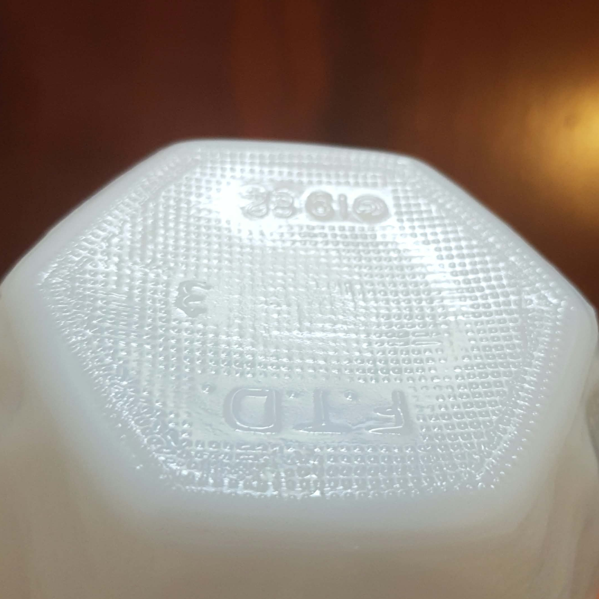 Close-up of the bottom of a translucent white glass vase with embossed FTD text, and numbers set against a dark brown background.