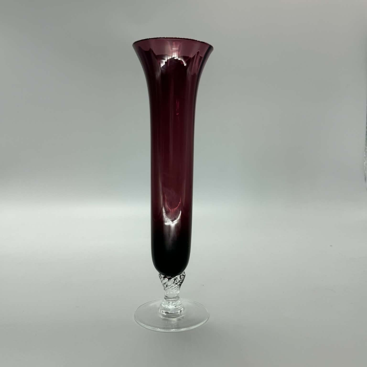 A tall flared glass vase with a deep burgundy-to-clear gradient and a clear glass pedestal base, photographed against a neutral gray studio background.