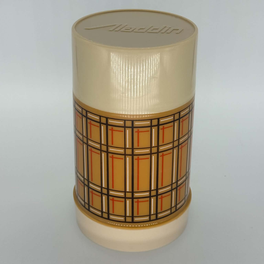 A vintage plastic cylindrical container with a cream-colored ribbed lid and base, featuring a central patterned band with a tan, orange, and black plaid design. The brand name 'Aladdin' is embossed on the lid.