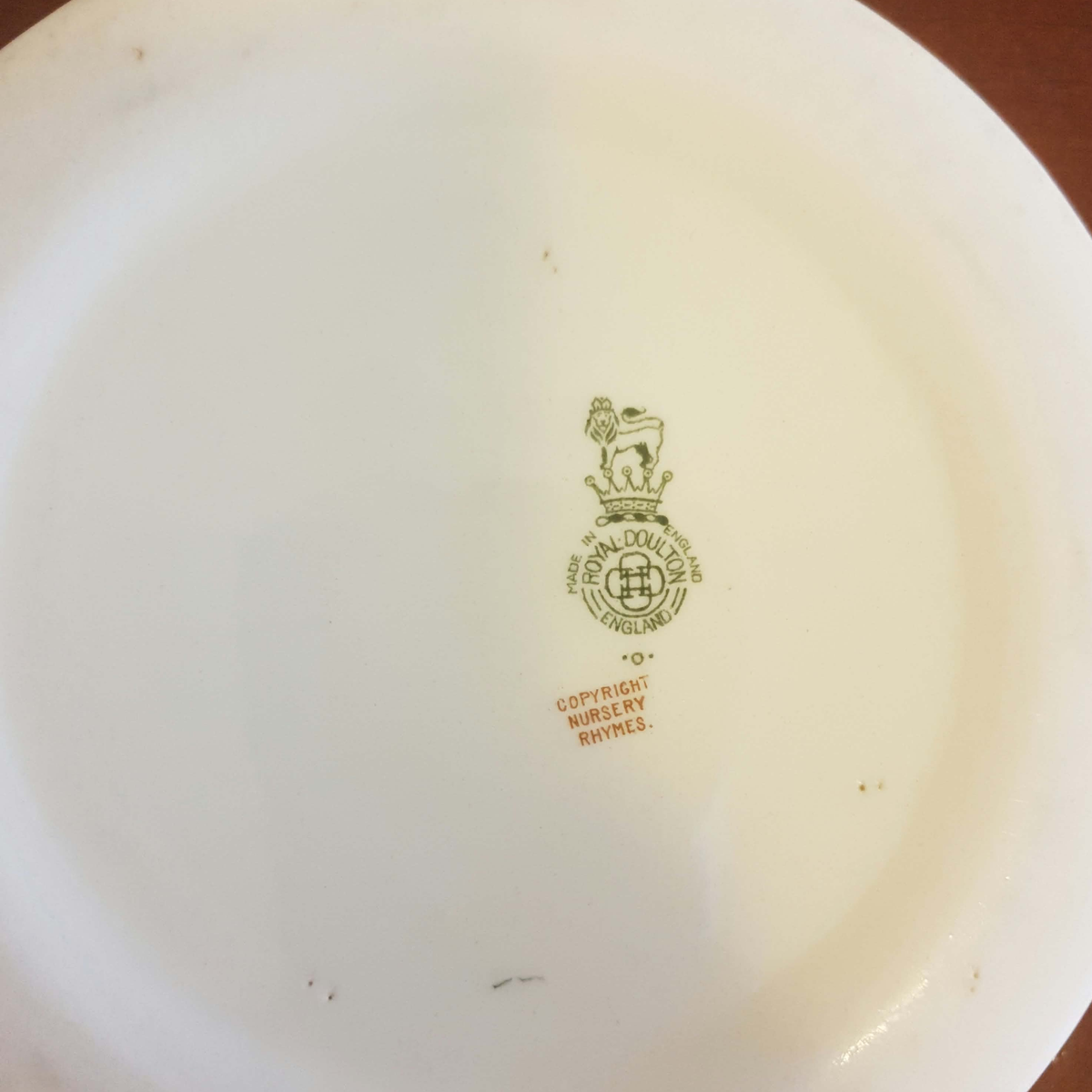 The underside of a white ceramic plate or dish, showing a green printed Royal Mint logo and copyright text for nursery rhymes.