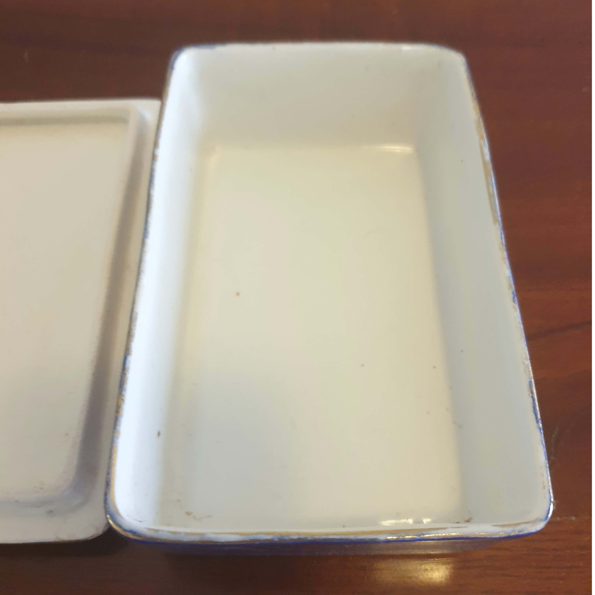 A white rectangular ceramic dish with a matching lid, shown on a brown wooden surface.